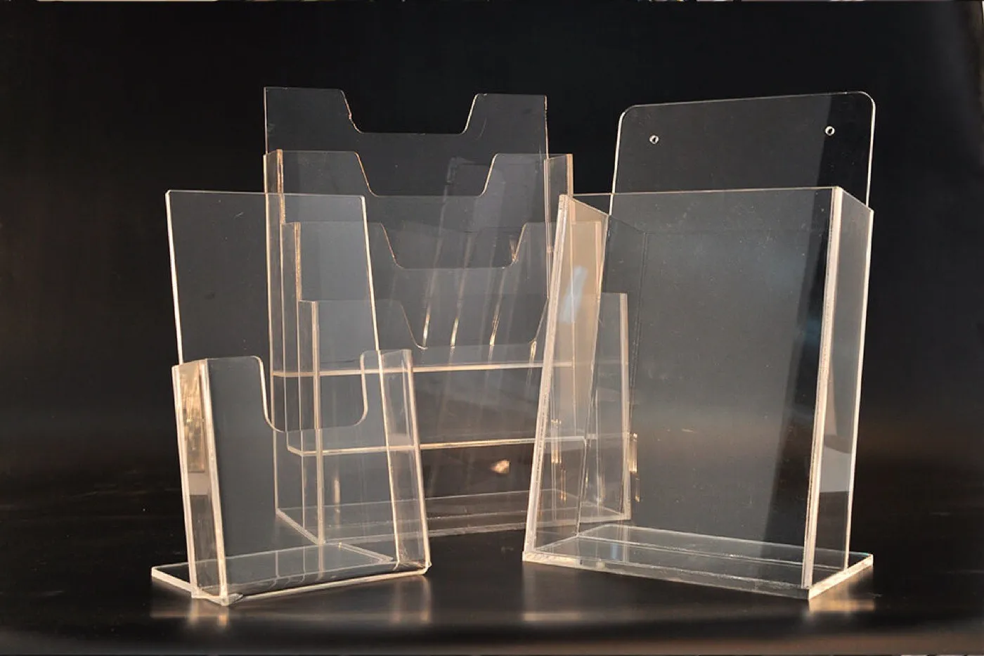 Clear acrylic brochure holders in several sizes on a dark background