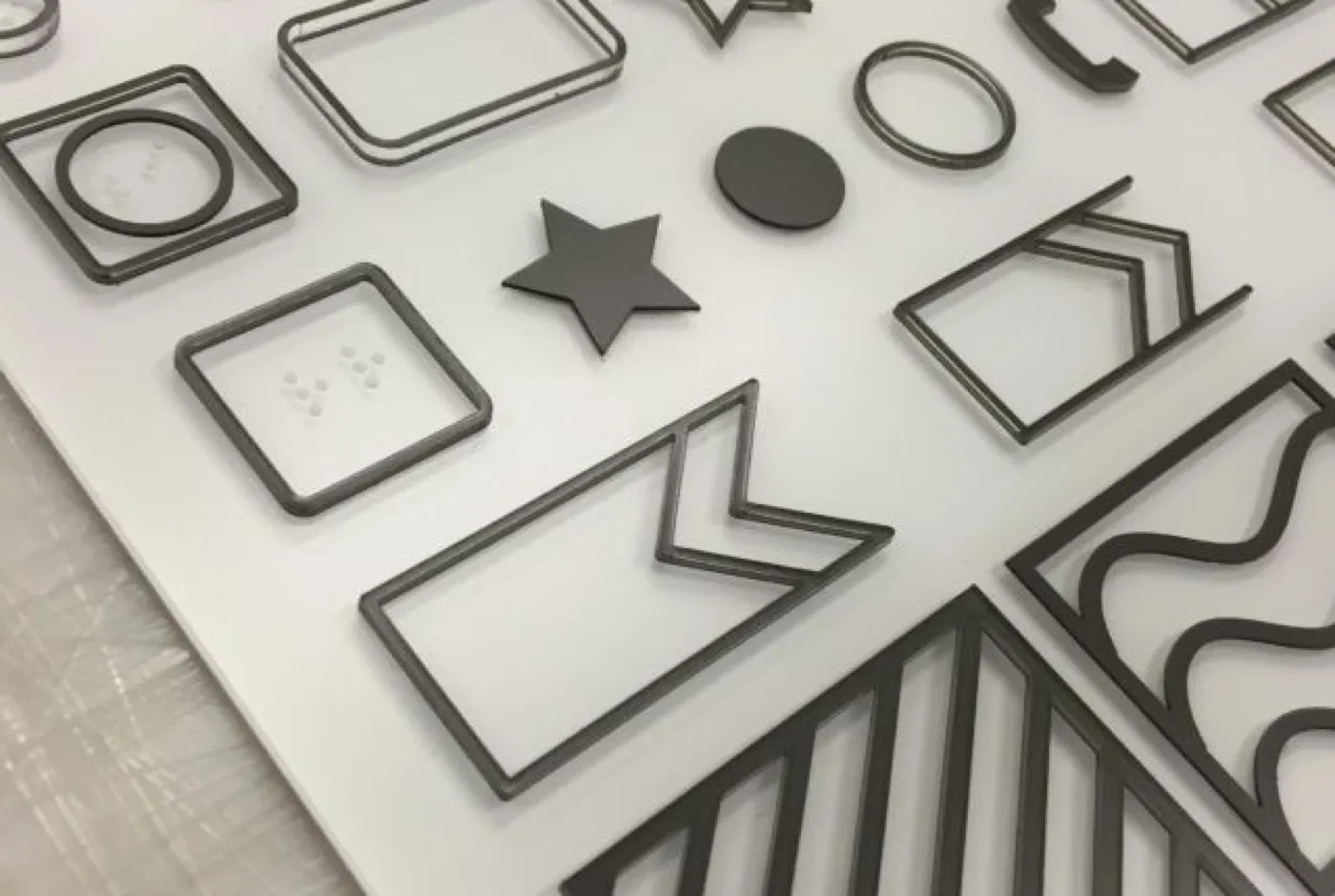 Laser-cut outline shapes including a star, a circle, squares and chevrons laid on a white panel